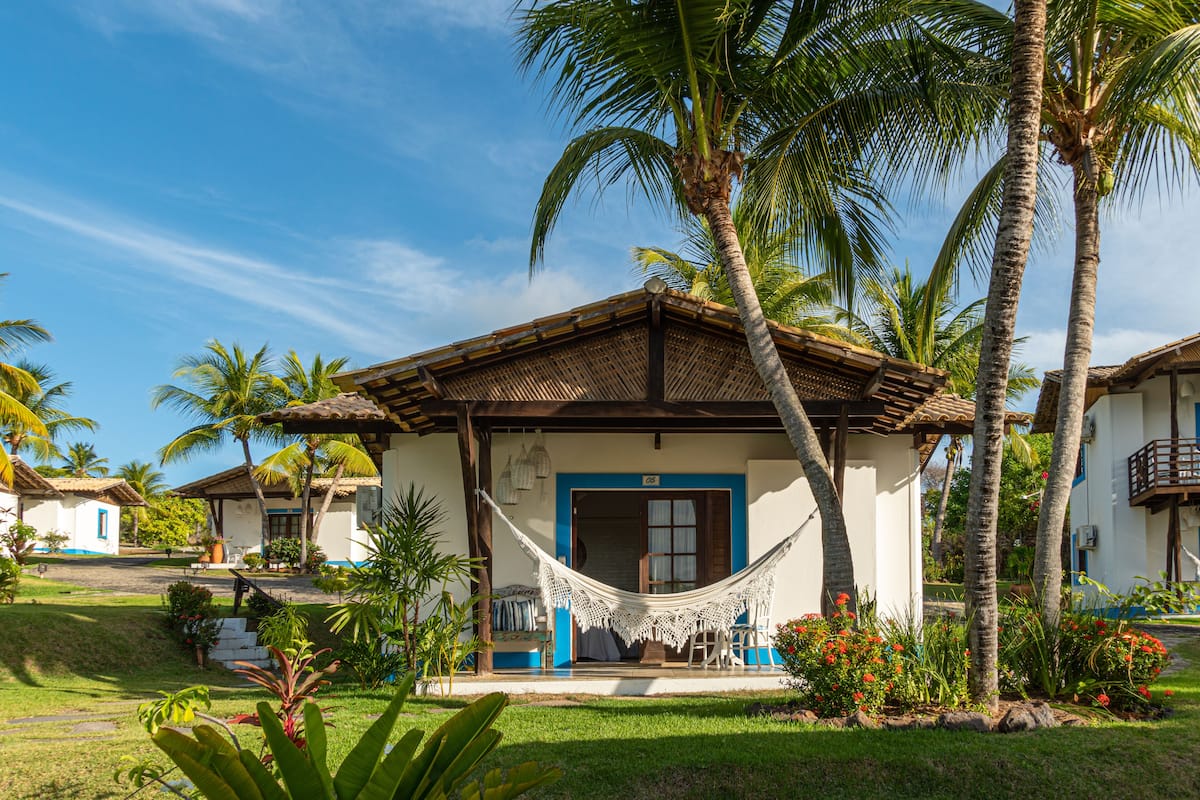 A white building with a blue door, surrounded by palm trees and a hammock.
