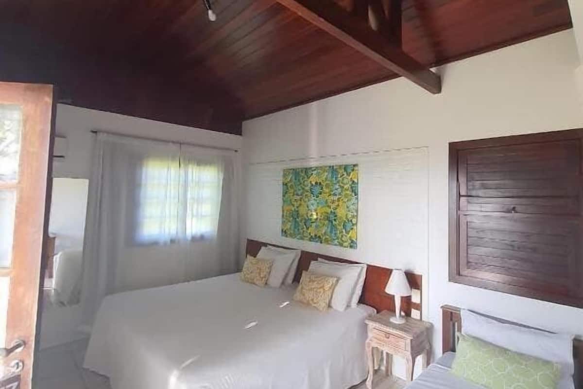 A room with two beds, a wooden ceiling, a painting on the wall, and a window with curtains.