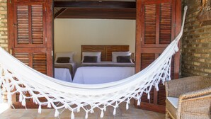 A hammock over a bed with wooden shutters, a wicker chair, and a brick wall. - Pousada Berro Do Jeguy (Tibau do Sul)