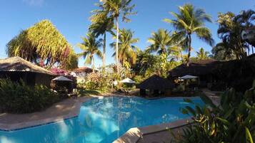 Relax by the serene pool surrounded by lush tropical vegetation and thatched-roof structures.