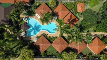An aerial view of a resort with a swimming pool, palm trees, and red-roofed buildings.
