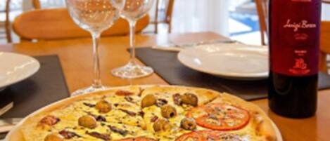 A pizza with toppings on a plate, a bottle of wine, and two glasses on a table.