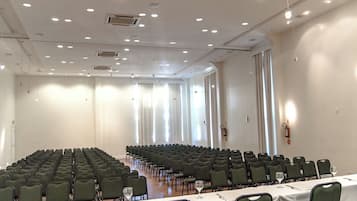 A conference room with rows of chairs, tables with white tablecloths, and large windows allowing natural light.