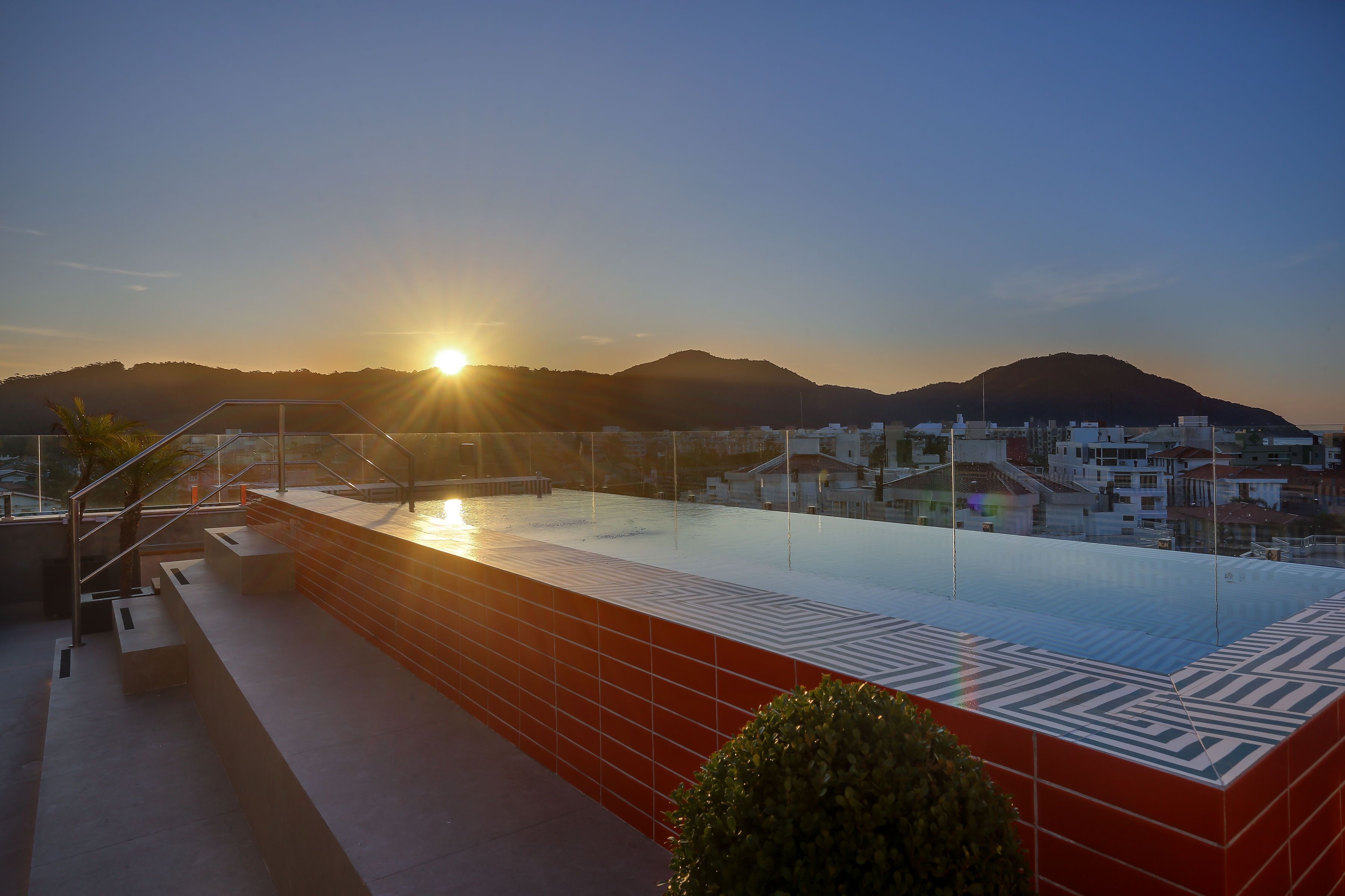 Une piscine sur le toit offrant une vue sur le paysage urbain et les montagnes au coucher du soleil.