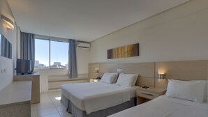 Habitación de hotel con dos camas, televisión, escritorio y ventana grande con cortinas.