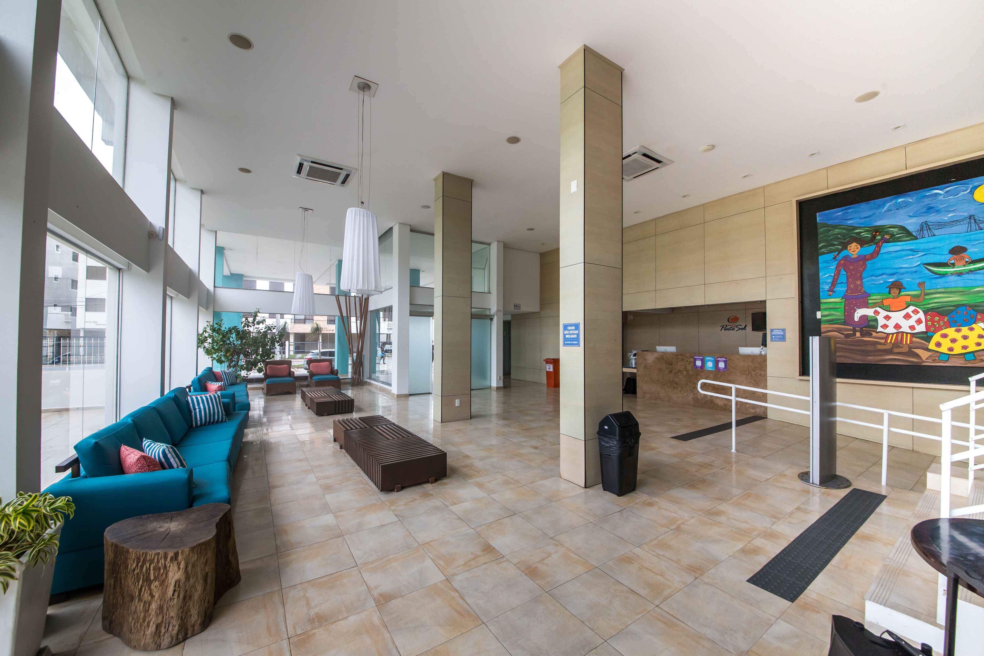 A spacious lobby with teal sofas, wooden tables, and a large mural depicting a tropical scene.