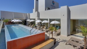 Un hotel moderno con piscina en la azotea, sillones de descanso y sombrillas.