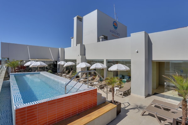 A modern hotel with a rooftop pool, lounge chairs, and umbrellas. - Hotel Porto Sol Ingleses (Florianópolis)