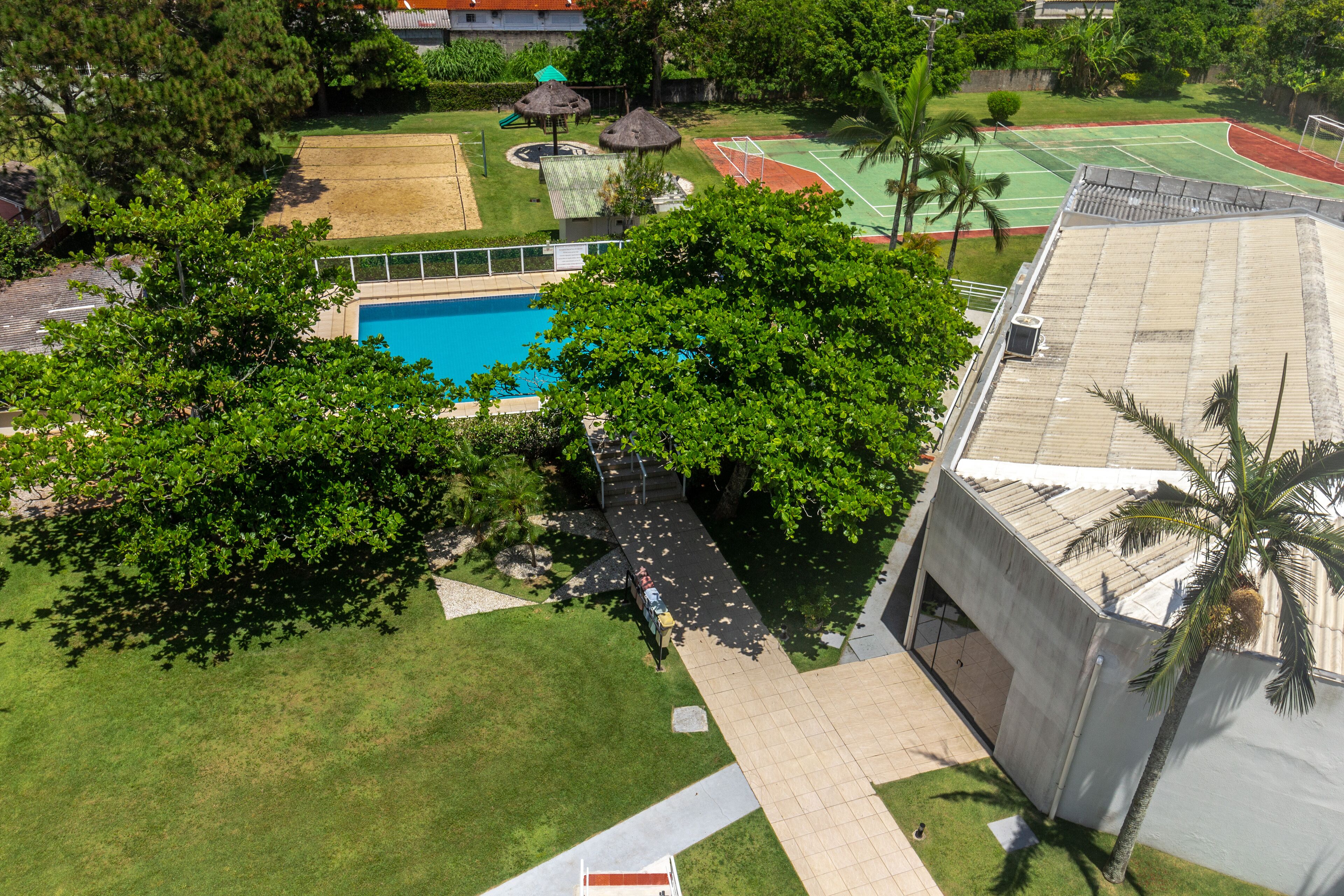 Vista aérea de una propiedad con piscina, canchas de tenis y un área techada con sombrillas de paja.