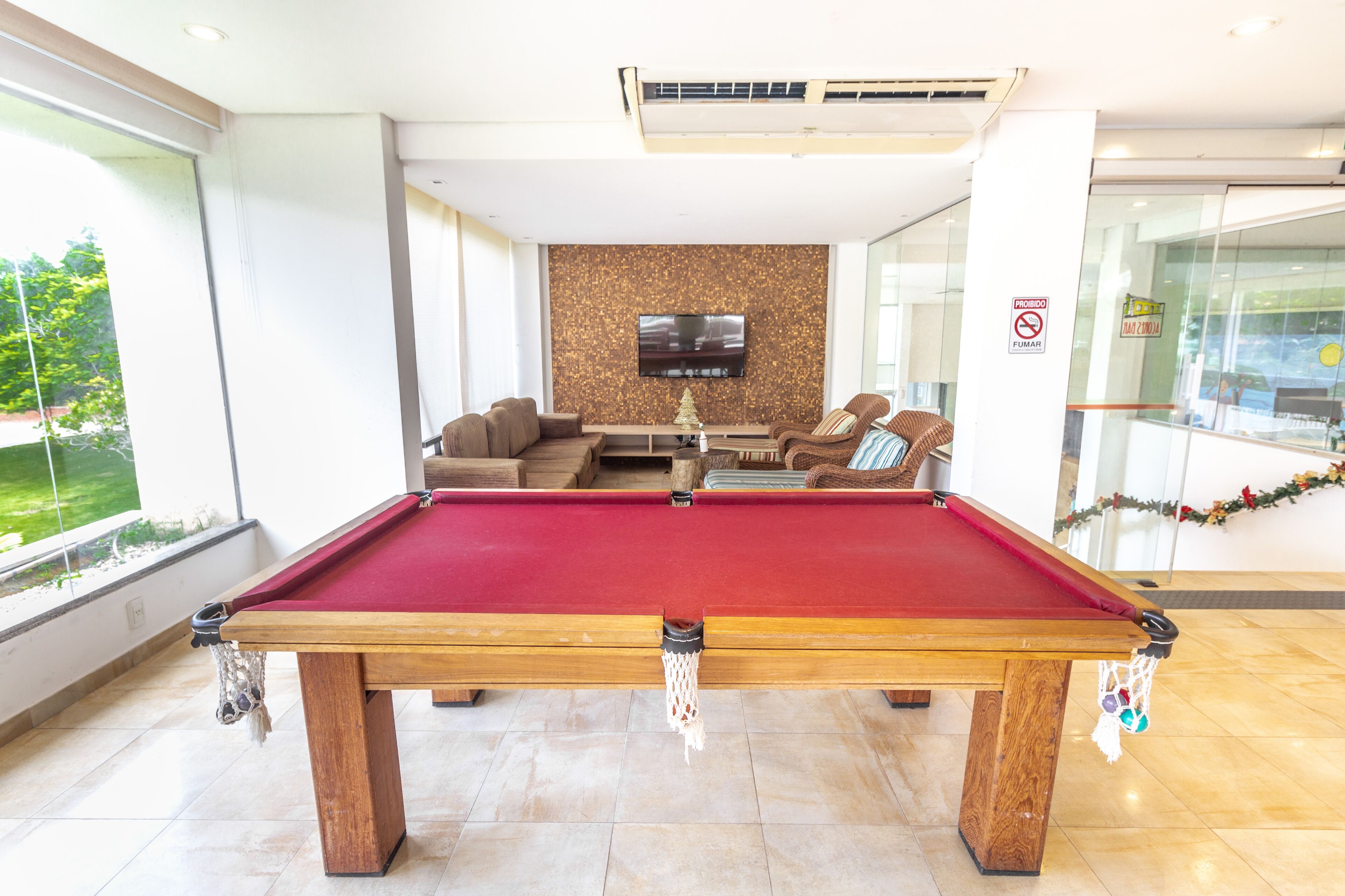 Une table de billard dans un espace intérieur moderne, avec une grande fenêtre, un téléviseur à écran plat fixé au mur et un coin salon avec des canapés.