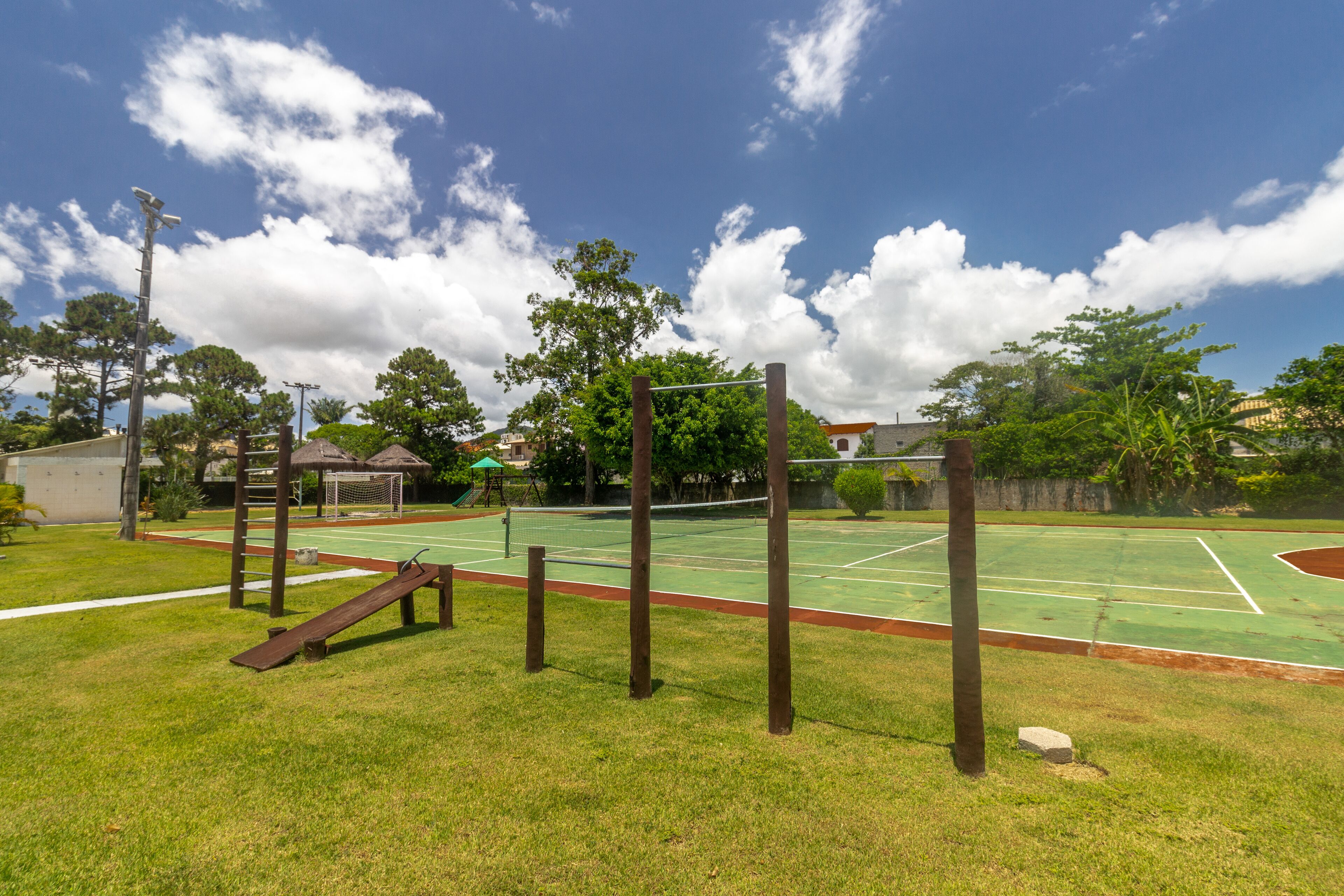 An outdoor basketball court with a wooden climbing structure, surrounded by grass and trees.