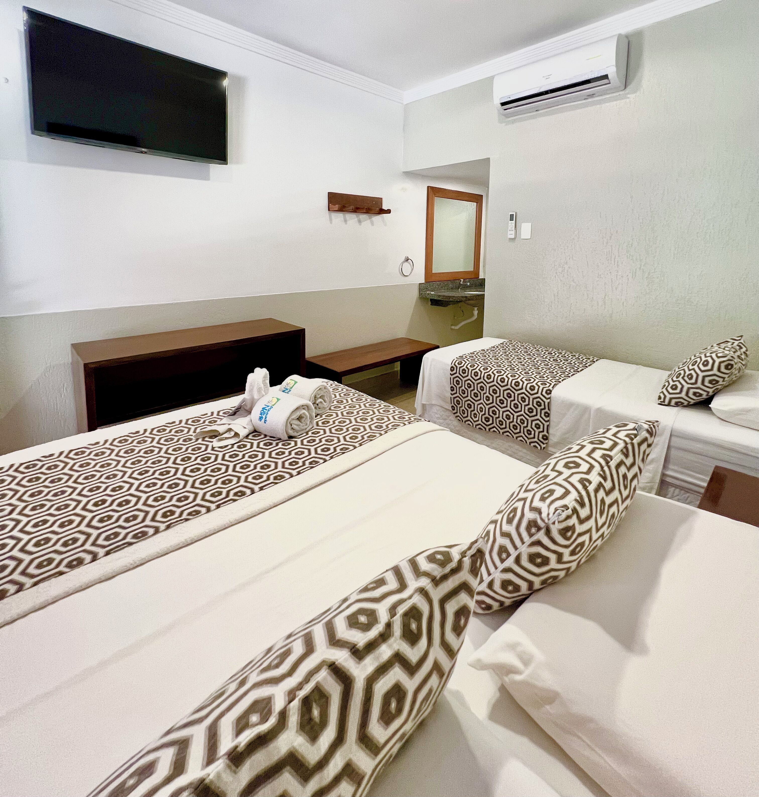 Une chambre d’hôtel avec deux lits, une télévision, un climatiseur et un petit bureau avec un miroir.