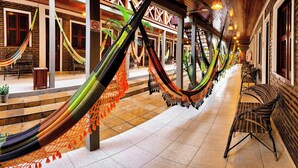 A corridor with hammocks hanging from the ceiling, wicker furniture, and a brick wall. - Rede Andrade Pousada do Norte (Jijoca de Jericoacoara)