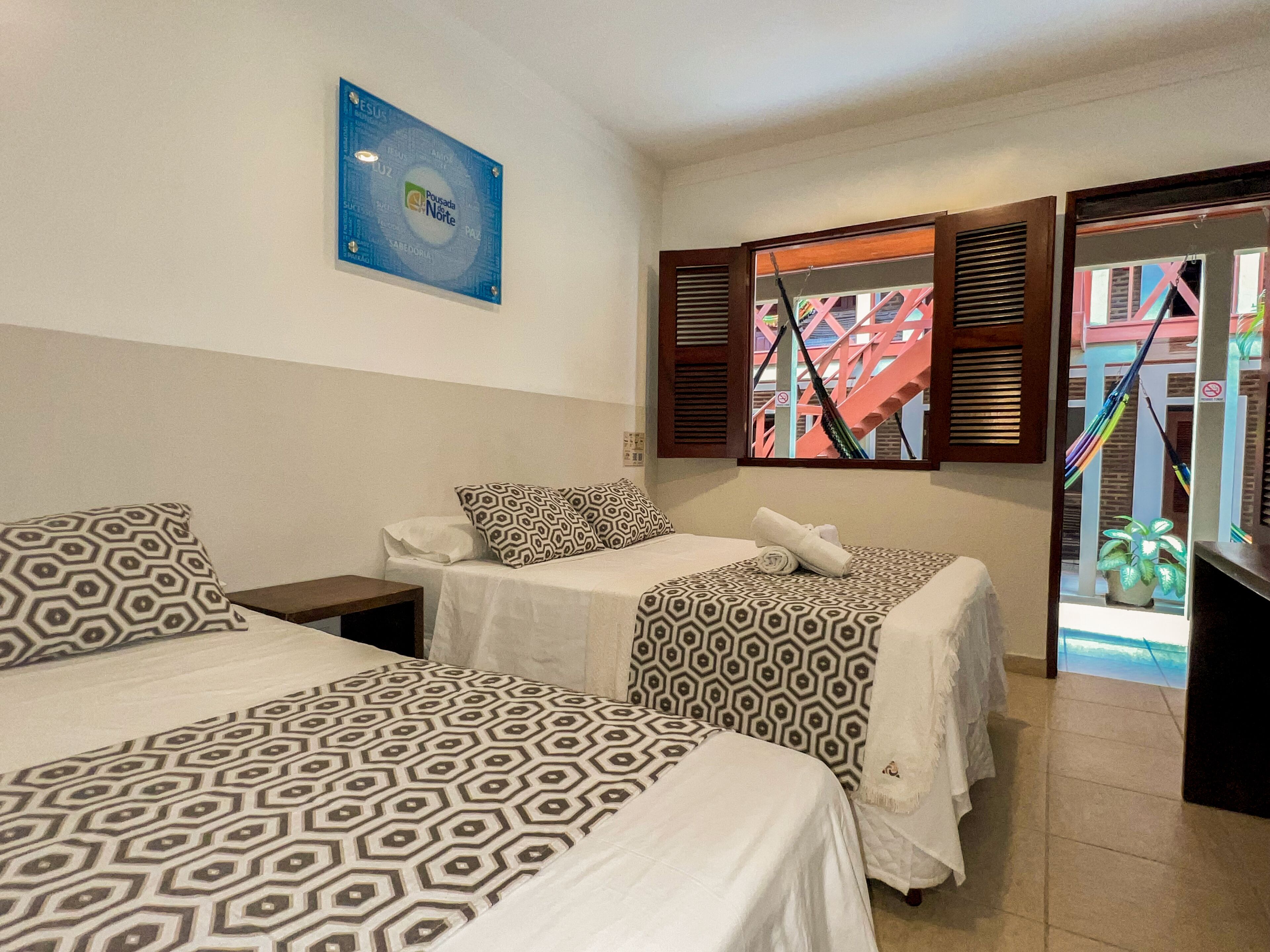 Habitación de hotel con dos camas, un cartel azul en la pared y vista a una escalera exterior.