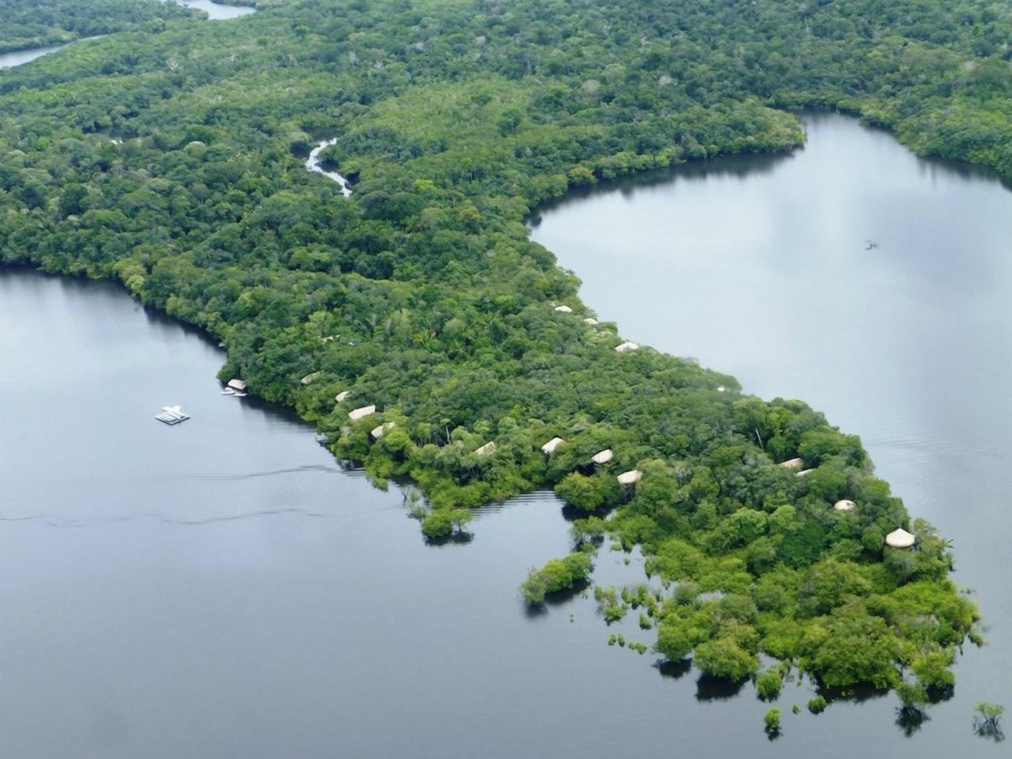 Vista aérea de uma ilha exuberante e verde com um rio serpenteando por ela e várias construções pequenas com telhados de palha.