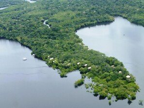 Une vue aérienne d’une île verdoyante, luxuriante, traversée par une rivière et parsemée de plusieurs petites constructions aux toits de chaume.