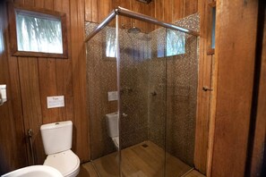 A wooden-paneled bathroom with a glass-enclosed shower, a toilet, and a window.