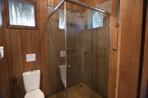 A shower enclosure with a glass door, wooden walls, and a visible toilet.