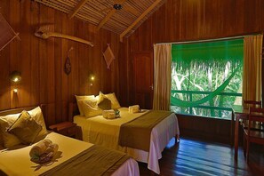 A wooden room with two beds, a window with a view of trees, and a chair.