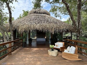 A wooden deck leading to a thatched-roof structure with a bed and seating area. - Juma Lodge - Hotel Selva (Careiro)