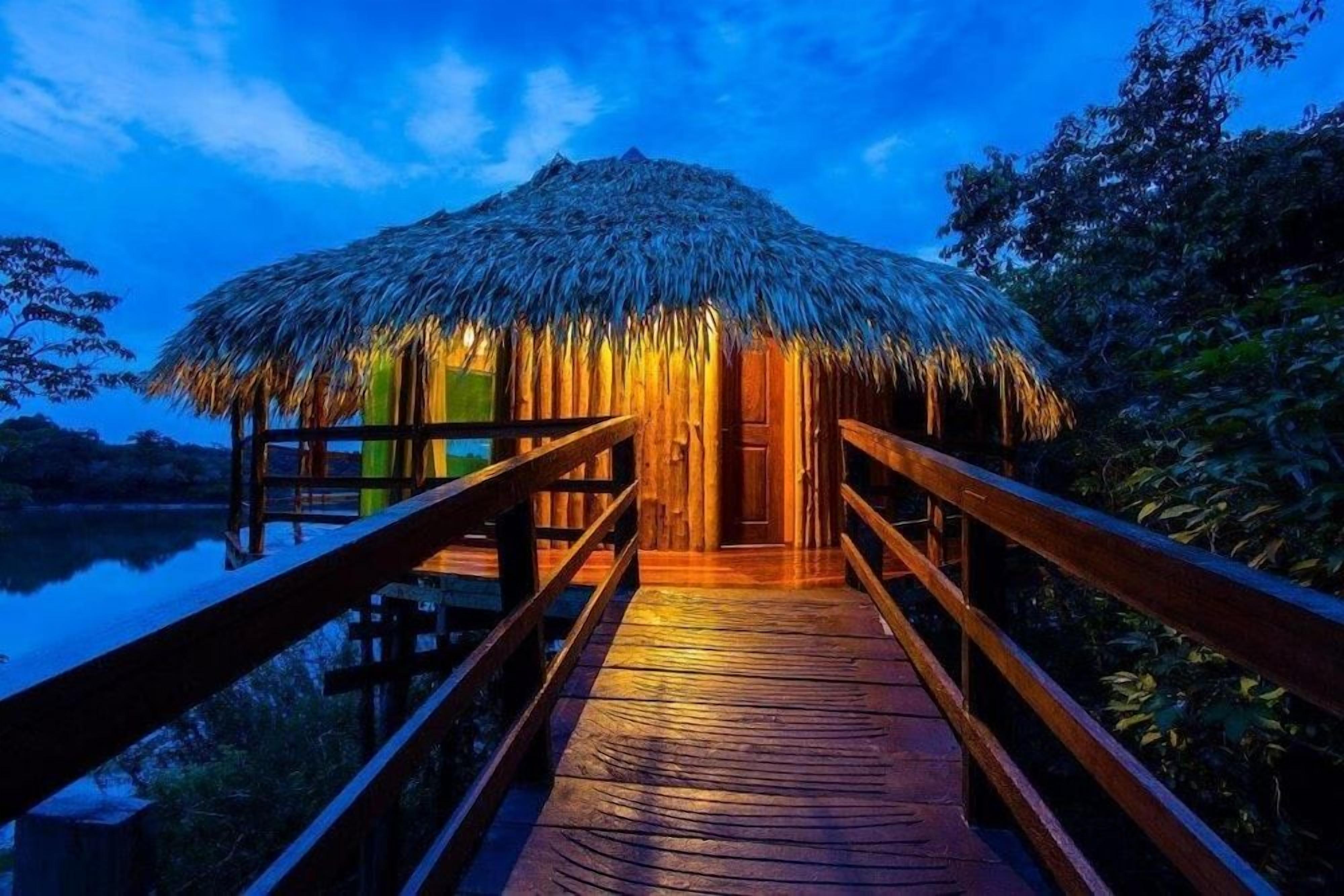 A wooden deck leading to a thatched-roof hut with a view of a body of water.