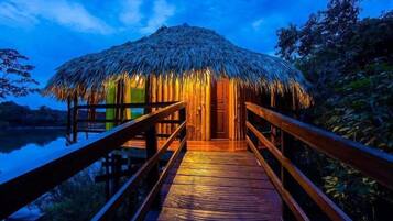 A wooden deck leading to a thatched-roof hut with a view of a body of water.