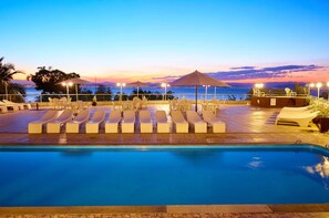 A poolside area with lounge chairs and umbrellas, overlooking a body of water at sunset. - Maria Do Mar Hotel (Florianópolis)