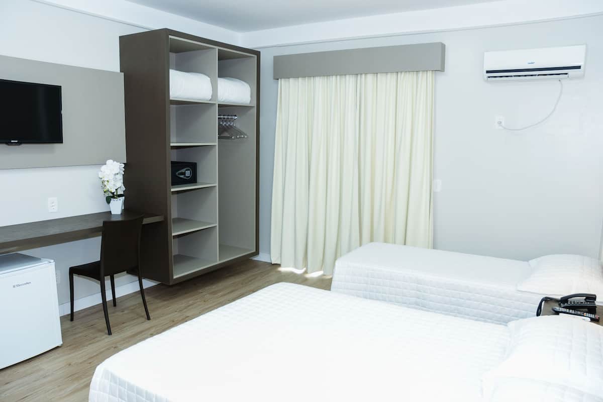 Een hotelkamer met twee bedden, een bureau, een kledingkast, een televisie en een airconditioning.
