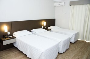 Une chambre d’hôtel avec deux lits simples, une table de chevet avec un téléphone et une télécommande, un climatiseur fixé au mur et une fenêtre avec des rideaux.