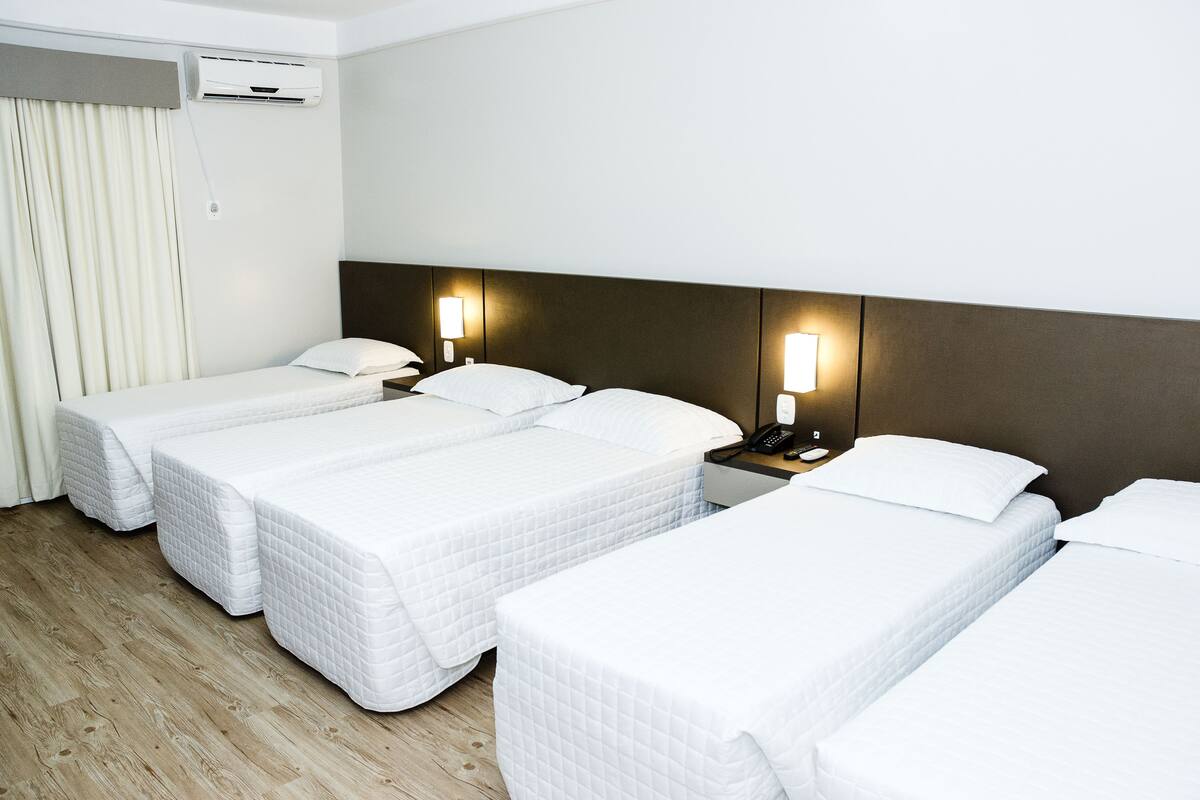 Een hotelkamer met drie eenpersoonsbedden, een nachtkastje met een lamp en een airconditioner aan de muur.