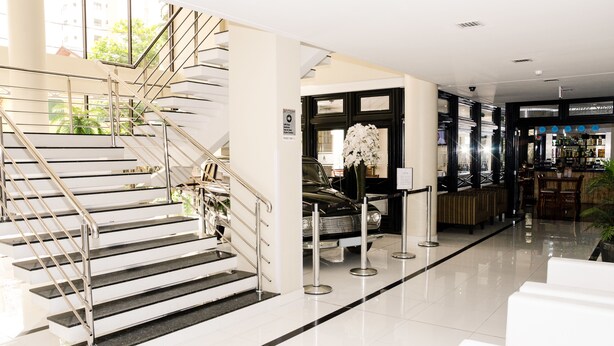 A modern hotel lobby with a staircase, a reception area, and a bar. - San Marino Cassino Hotel (Balneário Camboriú)