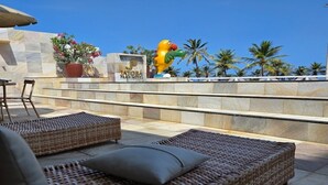 Outdoor wicker lounge chairs with cushions, a decorative parrot statue, and a view of palm trees. - Jatobá Praia Hotel (Aracaju)