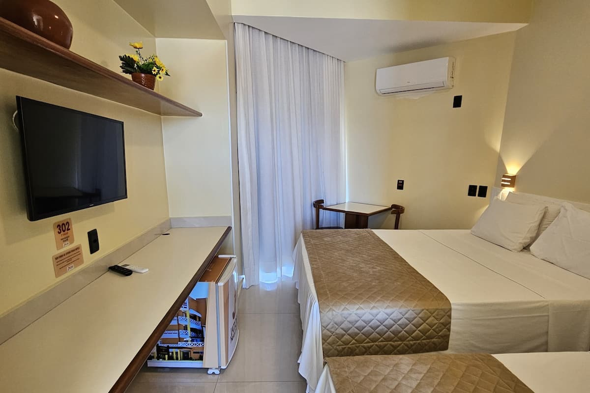 Habitación de hotel con televisión, cama, mesita de noche, una pequeña mesa y ventana con cortinas.