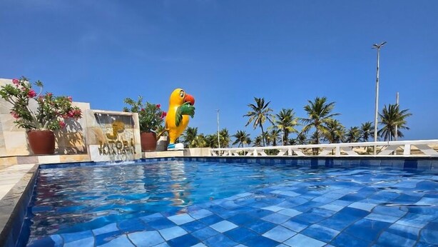A swimming pool with blue tiles, surrounded by palm trees and a decorative bird statue. - Jatobá Praia Hotel (Aracaju)