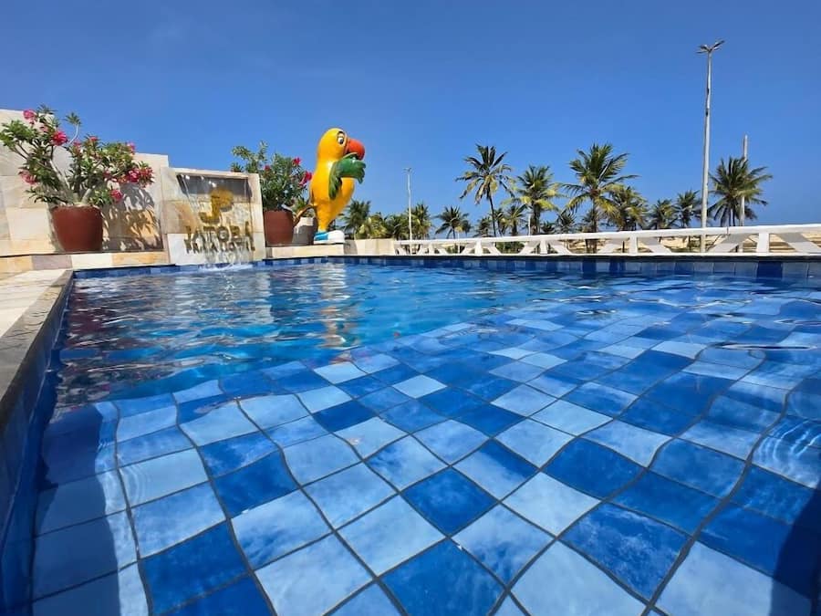 Ein Swimmingpool mit blauen Fliesen, umgeben von Palmen und einer dekorativen Vogelstatue.
