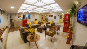 A lobby with a reception desk, sofas, and a coffee table. There is a Coca-Cola refrigerator and a television on the wall. - Jatobá Praia Hotel (Aracaju)