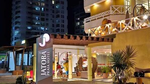 The exterior of the Jatoba Praia Hotel with a well-lit entrance, a covered outdoor seating area, and a view of the surrounding buildings. - Jatobá Praia Hotel (Aracaju)