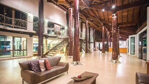 Un hall d’entrée spacieux, avec un canapé en cuir marron, une table basse en bois et un escalier doté d’une rampe en verre.