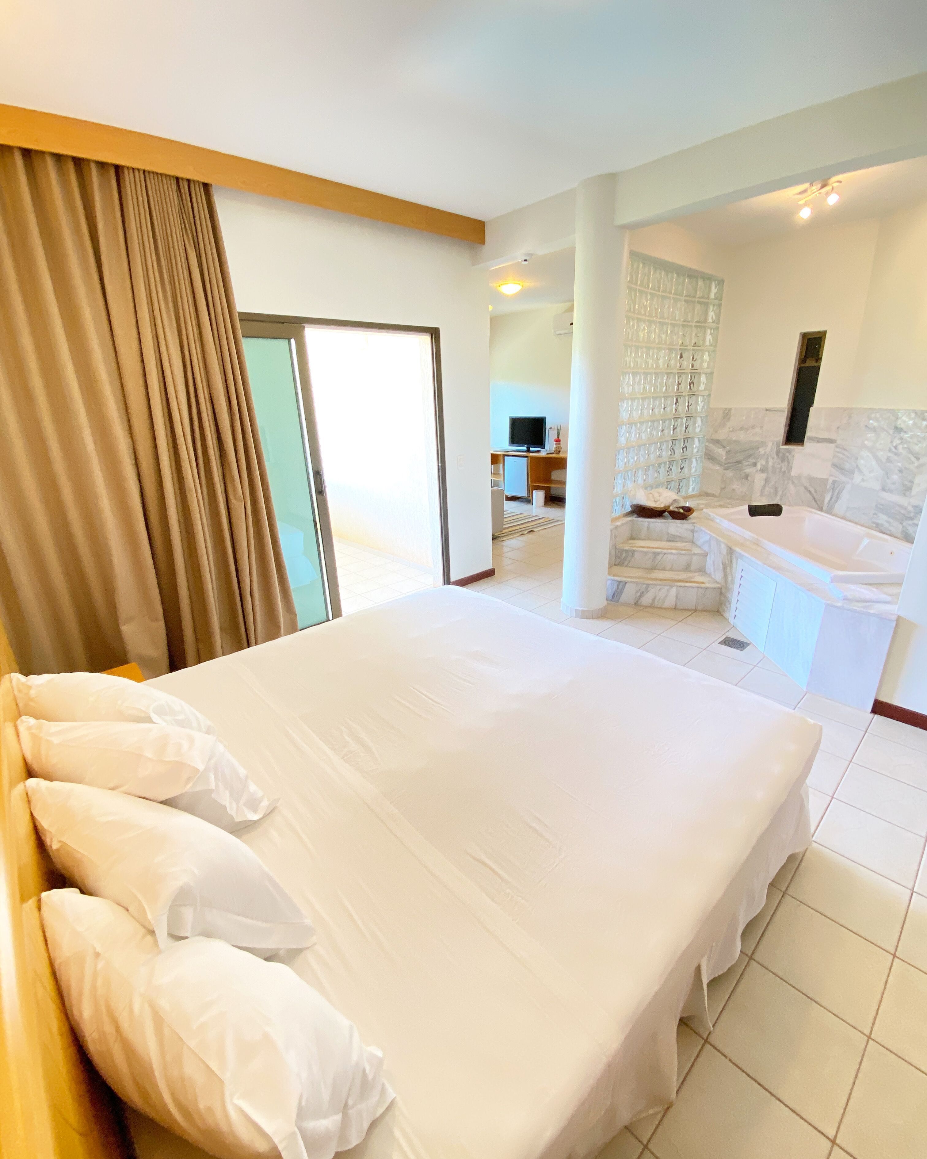 A hotel room with a large bed, a bathroom with a bathtub, and a living area with a TV.