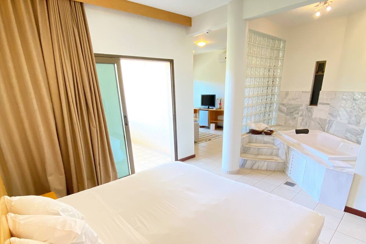 A hotel room with a large bed, a bathroom with a bathtub, and a living area with a TV.