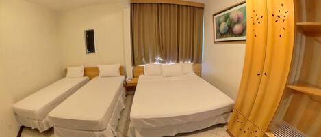 A hotel room with two single beds, a wooden wardrobe, a small table, and a window with curtains.