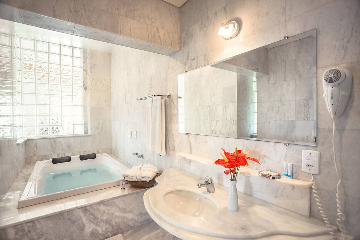 A modern bathroom with a large bathtub, a sink, a mirror, and a hairdryer.
