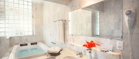 A modern bathroom with a large bathtub, a sink, a mirror, and a hairdryer.