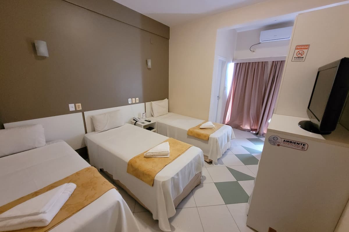 Habitación de hotel con dos camas individuales, un escritorio con silla, televisor y un cartel que indica prohibido fumar.