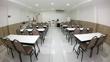 Un salón de conferencias con varias mesas y sillas, paredes blancas y piso de baldosas.
