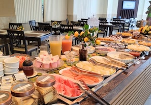 Un buffet proposant une variété de plats et de boissons, notamment des fruits, des fromages et un distributeur de jus.