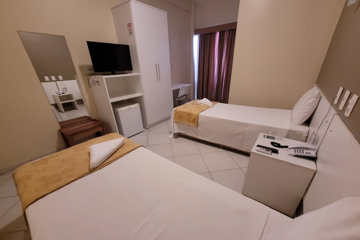 Habitación de hotel con dos camas, un televisor en un estante, un escritorio con teléfono y control remoto, y un armario.