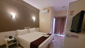 A hotel room with a large bed, a bedside table with a phone and a lamp, an air conditioning unit, a television, and a sign indicating the room is disinfected. - Sandrin Praia Hotel (Aracaju)