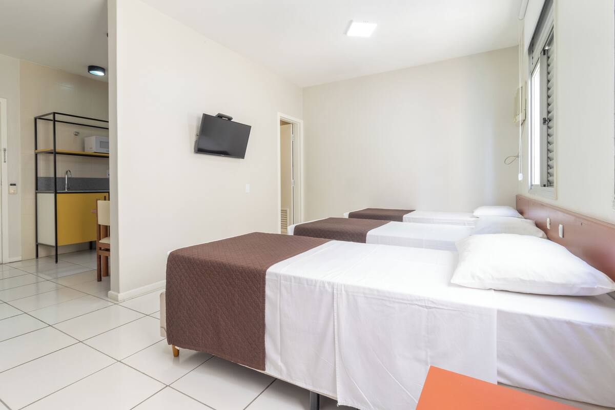 A hotel room with three beds, a TV on the wall, and a kitchenette in the background.