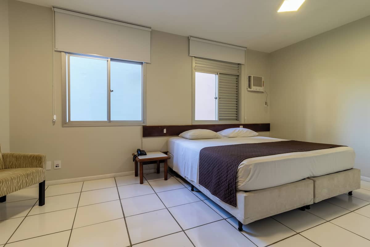 A bedroom with a bed, a chair, and two windows.